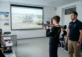 Інструктор спостерігає, як учень цілиться з навчального гранатомета по проєкції танка в умовах інтерактивного тиру