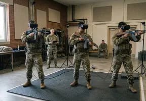 Троє військовослужбовців у шоломах віртуальної реальності відпрацьовують тактичні навички зі зброєю у тренувальному приміщенні
