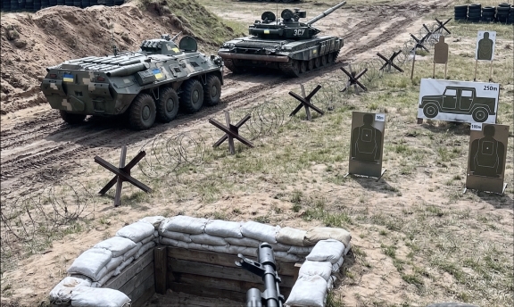 Тактичне поле бою з окопом на передньому плані, протитанковими їжаками, мішенями та бронетехнікою, включаючи танк і БТР